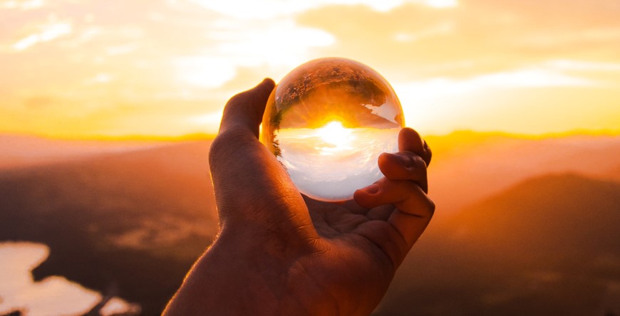 Hand holding Crystal Ball up against the setting Sun