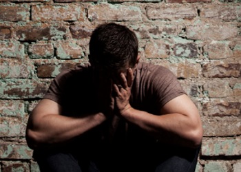 Man crouched at wall with head in hands