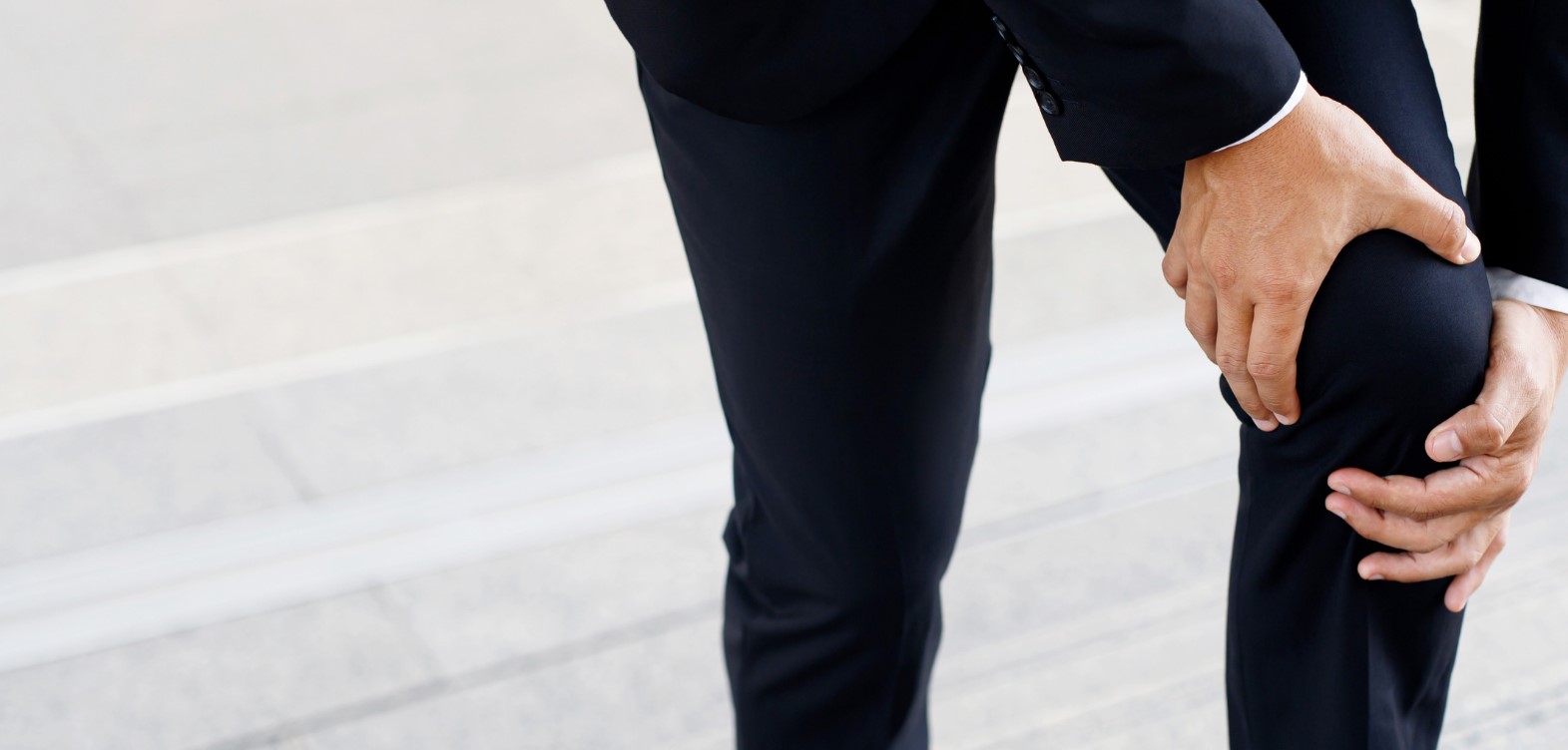 Male in dark suit holding painful knee with two hands