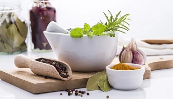 Various herbs and spices, including black pepper and turmeric in bowls, on chopping board, on table