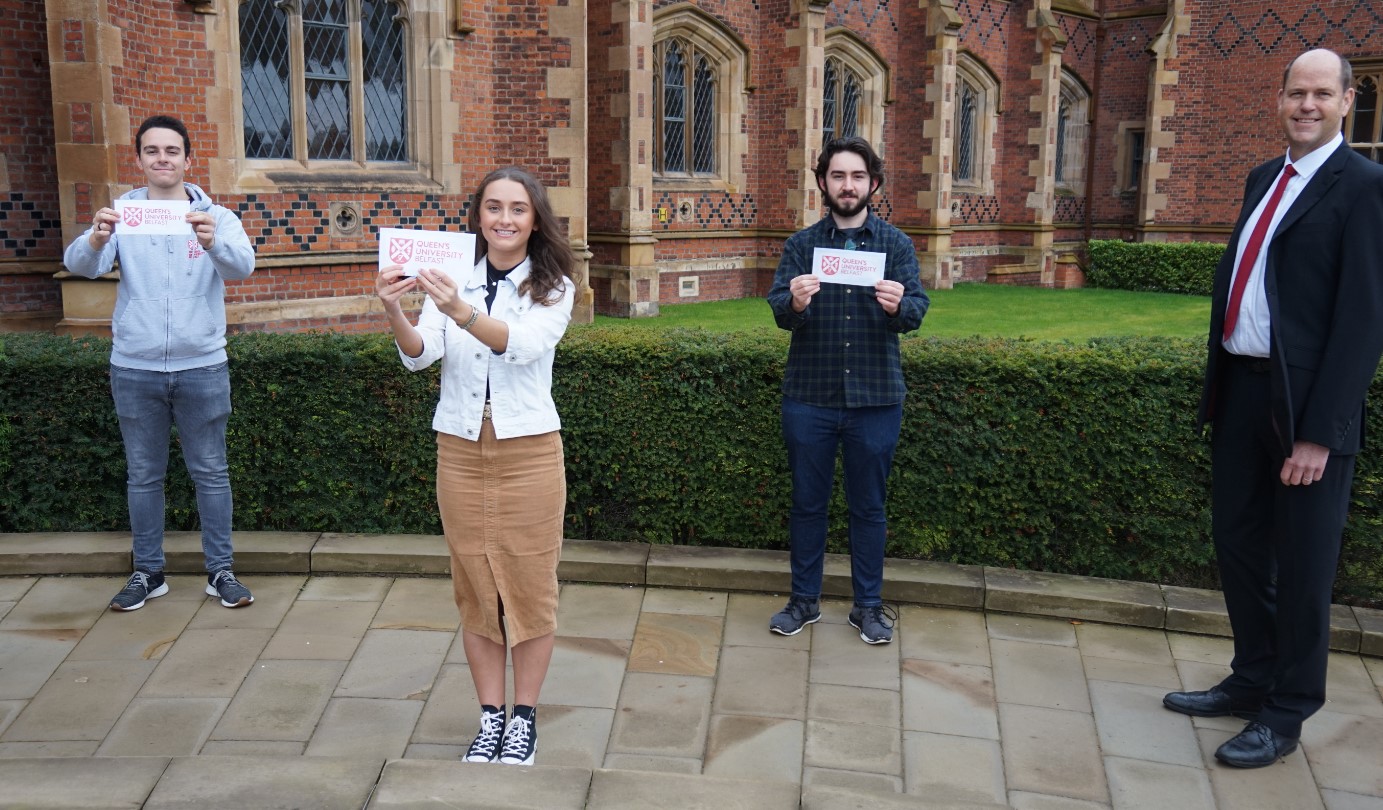 Three students standing in front of Queen's Lanyon Building holding aloft awards from Choice Housing, with Ted Jensen from University's Widening Participation Unit