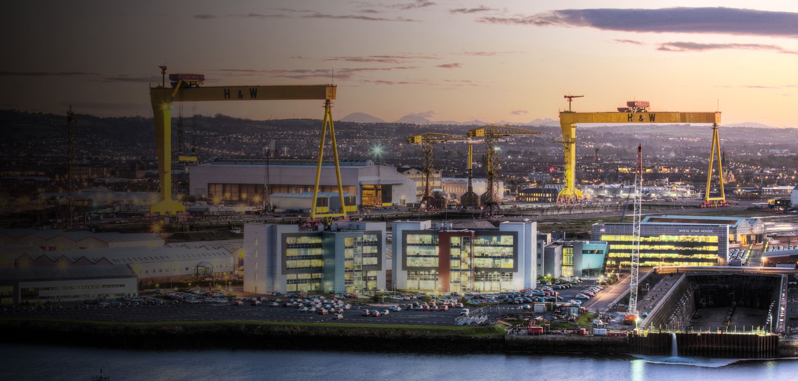 Belfast evening skyline showing shipyard cranes and buildings in foreground and Mourne Mountains in distance