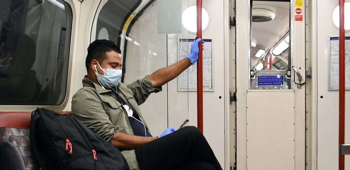 Man in mask and protective gloves sitting on London Underground tube