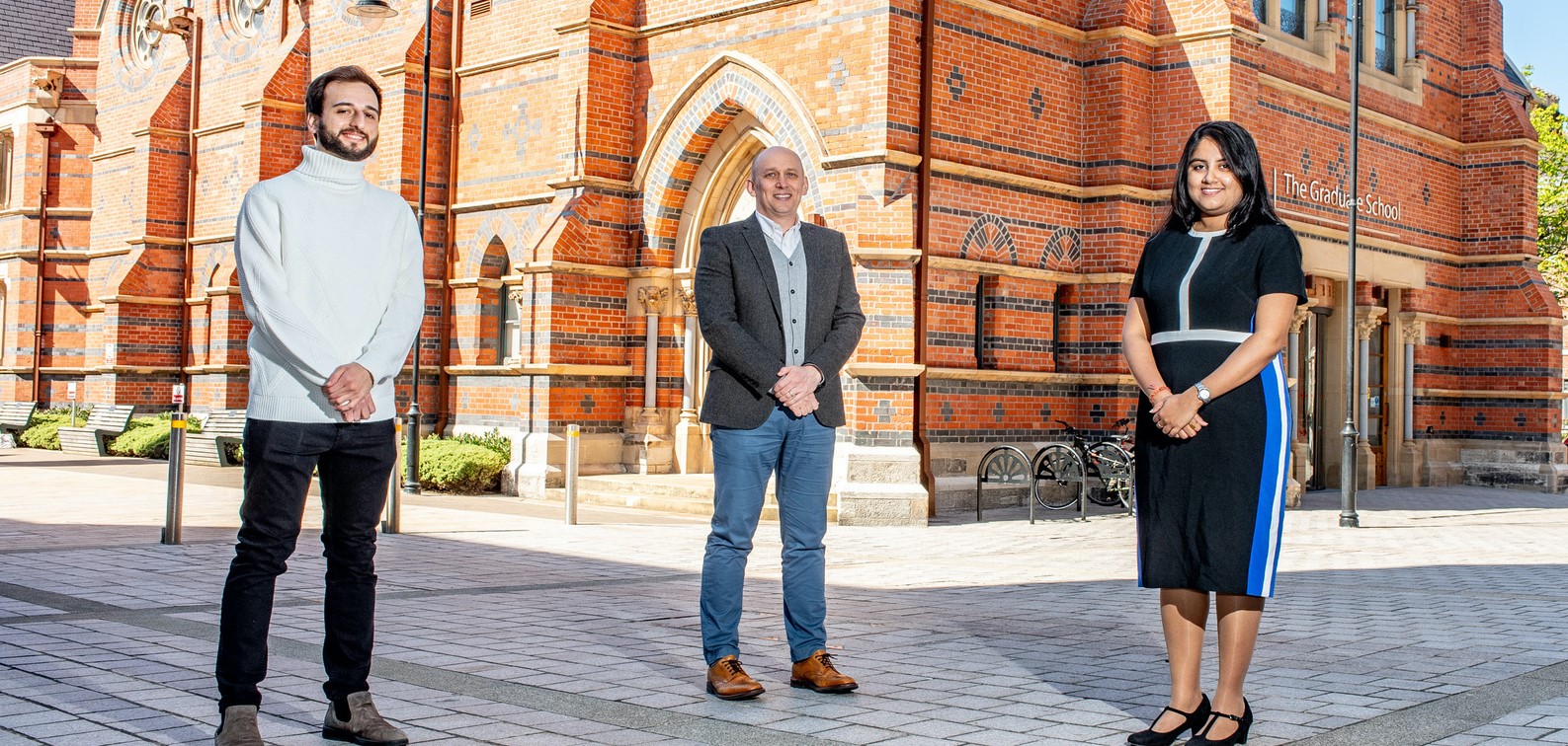 Two men and one woman standing outside red-bricked Graduate School at Queen's University Belfast