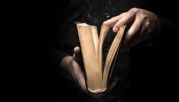 Cropped hands opening a book against dark background 