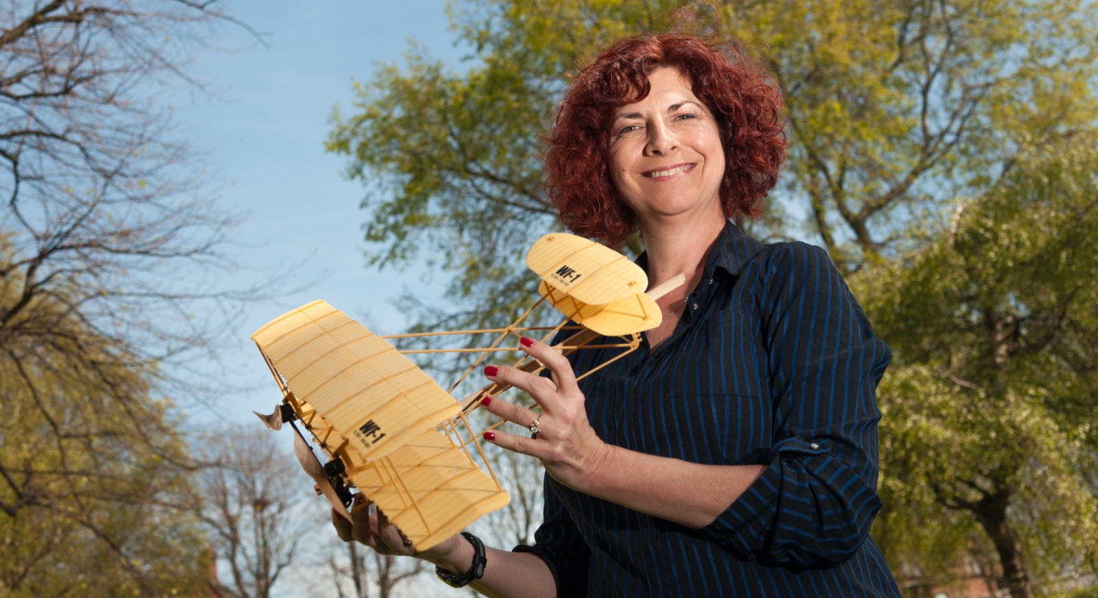 Dr Dani Soban holder model aircraft, standing in a park with trees in background
