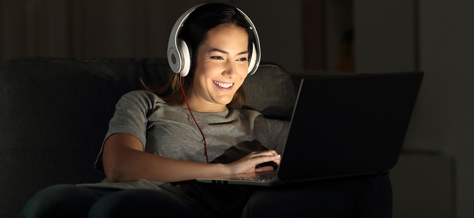 Happy young woman wearing headphones working at laptop computer