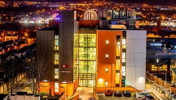 Brightly lit view of Precision Medicine Centre (PMC) at Queen's with Belfast city nightscape in background
