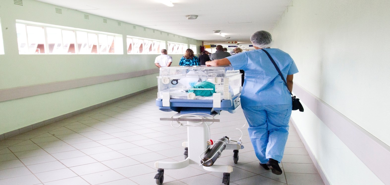 Nurse walking alongside ventilator in hospital corridor 