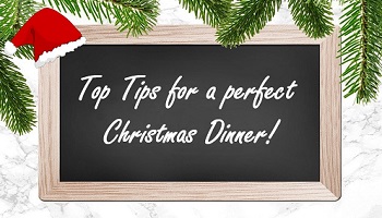 Yuletide sign with wording Top Tips for a perfect Christmas Dinner written on blackboard with tree branches and Santa hat in background