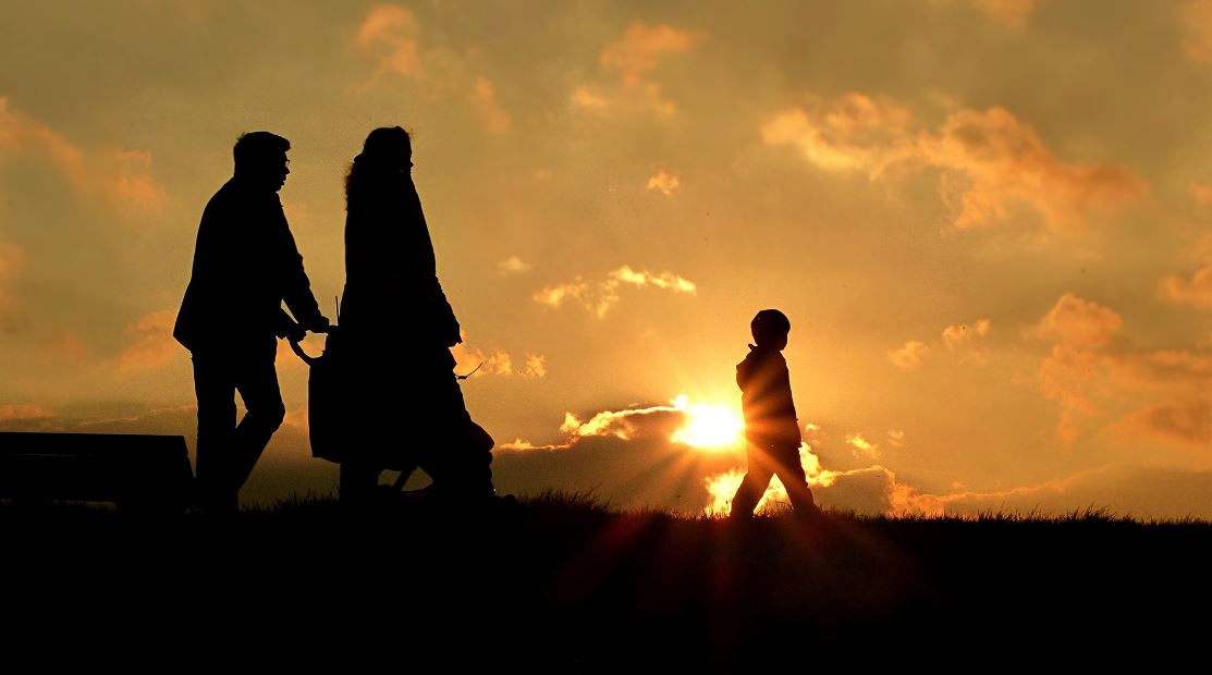 Man pushing pram with woman and young child silhouetted by sunset